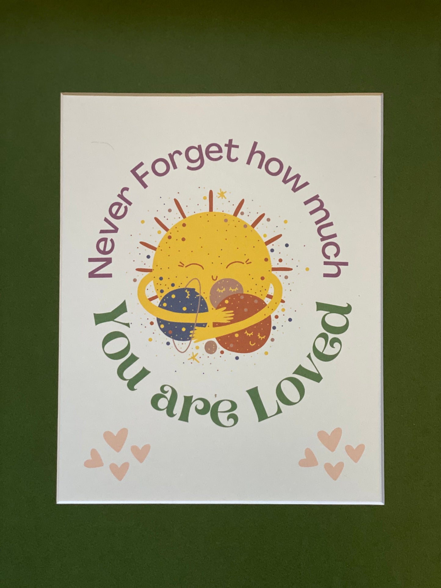 Unframed PunkerDoodle® 'Never Forget How Much You Are Loved' wall art print displayed with a Basque Green 11x14 mat, featuring a smiling sun hugging two planets with surrounding pink hearts and colorful text.