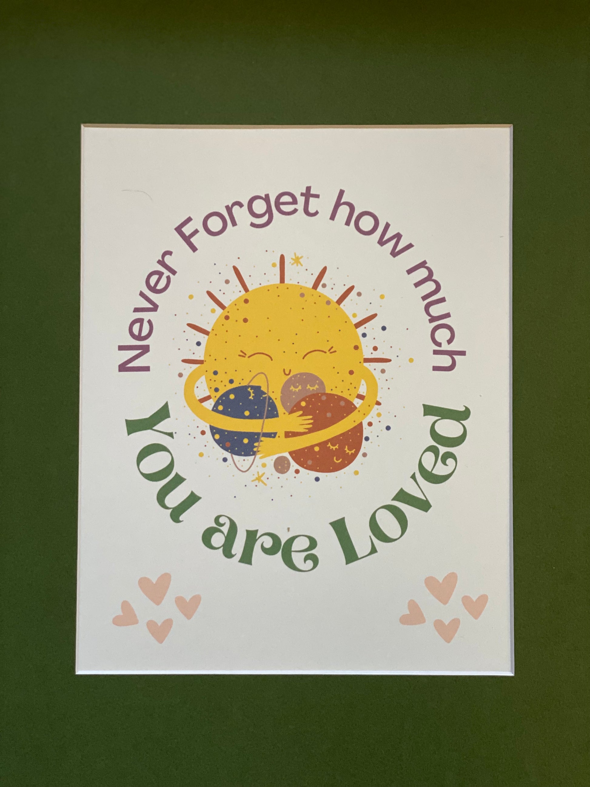 Unframed PunkerDoodle® 'Never Forget How Much You Are Loved' wall art print displayed with a Basque Green 11x14 mat, featuring a smiling sun hugging two planets with surrounding pink hearts and colorful text.